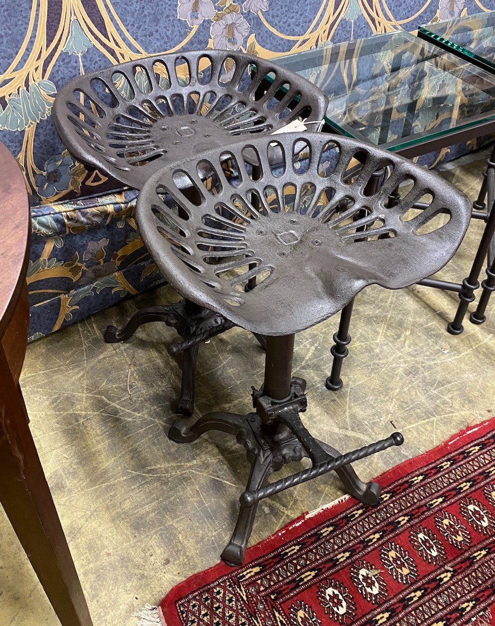 A pair of cast iron tractor seat stools, width 46cm, height 65cm
